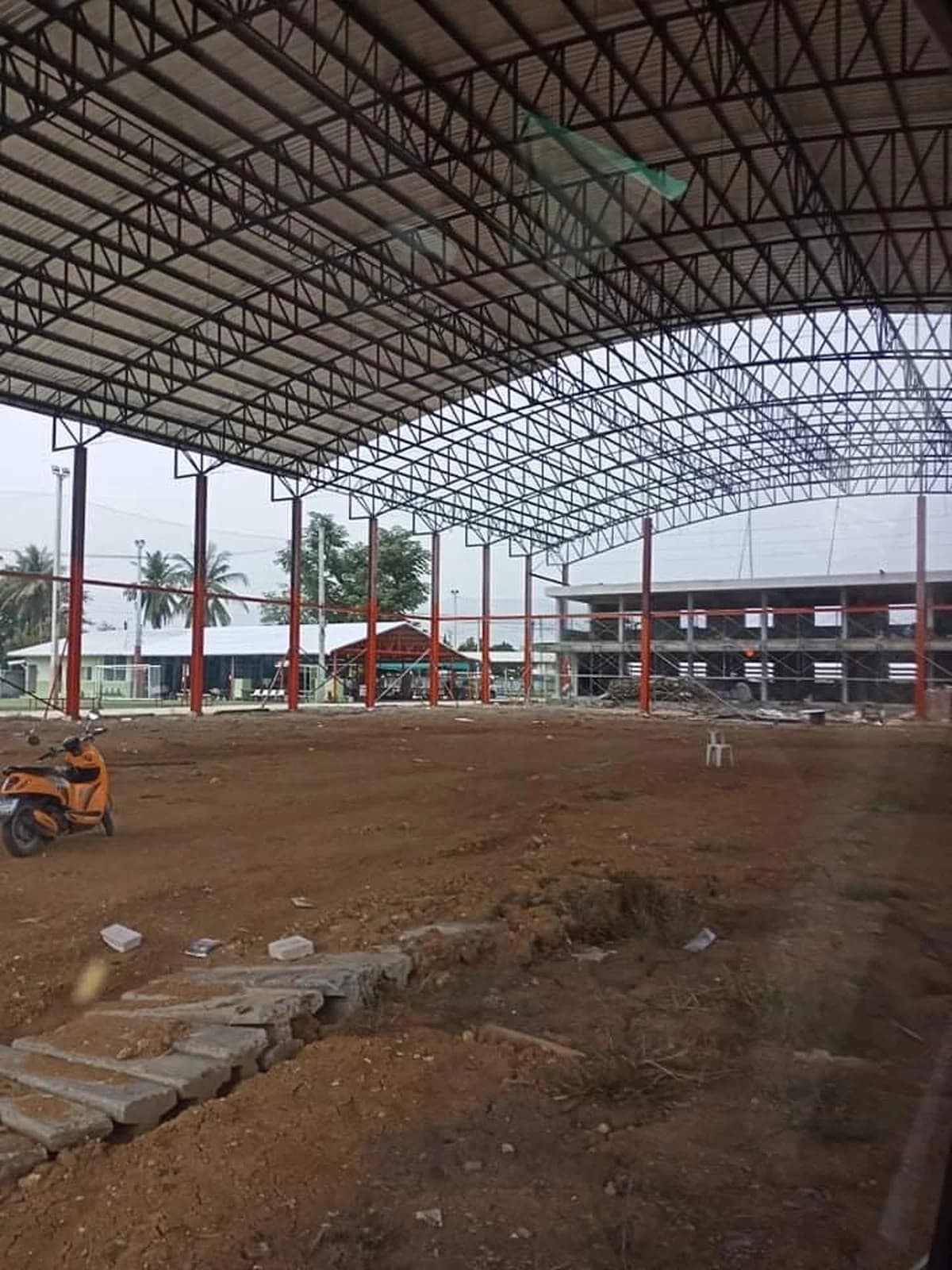 ภายในโครงสร้างเสาเหล็กสีแดงและหลังคาเมทัลชีท พื้นดินยังไม่ปูสนาม มีแผ่นคอนกรีตวางกองด้านหน้า