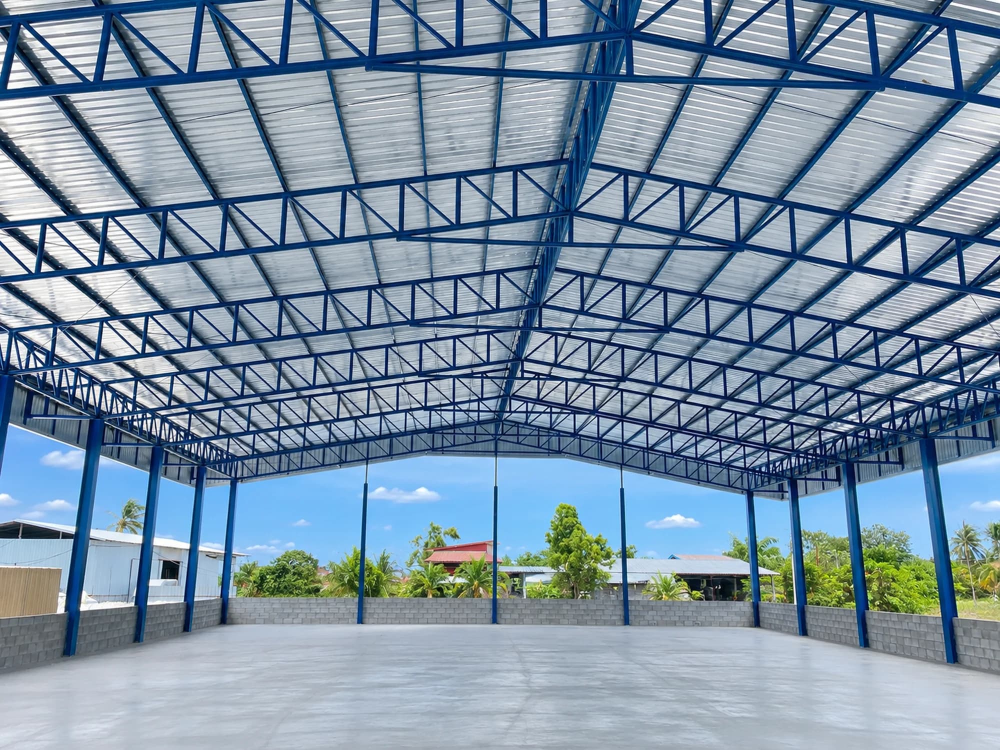 ภายในโรงงานโครงสร้างเหล็กสีน้ำเงินหลังคาเมทัลชีท พื้นคอนกรีตเรียบ และผนังเตี้ยคอนกรีตบล็อก — โครงการ Wellgoodnet
